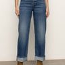 Wearing Sanctuary Clothing’s soleil 90s straight jeans in indigo medium with rolled cuffs and brown suede ankle boots, the person stands on a neutral floor against a plain off-white wall.