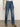 A person wears Sanctuary Clothing soleil 90s straight jeans in indigo medium with a light shirt and brown heeled ankle boots, standing on a gray floor against a plain light background. The image is cropped from the shoulders down.