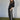 A woman stands on a green carpet, hands in pockets, wearing Sanctuary Clothing’s coated twill track pant in black with white side stripes and a black leather jacket, looking confidently at the camera against a plain light background.