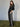 A woman stands on a green carpet, hands in pockets, wearing Sanctuary Clothing’s coated twill track pant in black with white side stripes and a black leather jacket, looking confidently at the camera against a plain light background.