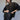A woman poses against a plain background in the Sanctuary Clothing club varsity jacket in midnight olive, styled with a black leather mini skirt. She has long, wavy hair and looks to the side with one hand on her waist.