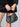 A person wears the Sanctuary Clothing quilted velvet mini skirt in black and holds a small black handbag with shiny silver studs, standing against a neutral background.