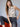 A woman with long, light brown hair and bangs sits on an orange chair, confidently wearing the Sanctuary Clothing fuzzy leopard shell mother leo top and black high-waisted jeans with a black belt against a plain background.
