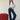 A woman with long light brown hair stands barefoot on a textured carpet, wearing Sanctuary Clothing’s soleil 90s straight jeans in indigo dark raw rinse with a white t-shirt and brown belt, beside a red ottoman against a plain background.