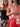 Two women stand side by side; one wears a black tube top and patterned skirt, while the other wears Sanctuary Clothing™s relaxed vacation shirt sunny riviera in beige and red with red pants. Both accessorize with gold jewelry and wear their hair loose.