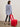 A woman wears the Sanctuary Clothing x PEANUTS 75th Anniversary "the doctor is in shirt blue and white stripe," styled with black jeans and heels, as she stands with a modern red chair in a minimalist room.