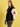 A woman with long brown hair wears the Sanctuary Clothing x PEANUTS 75th Anniversary 75 varsity jacket in black and white, paired with black jeans, against a plain yellow background.
