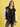 A person stands against a yellow background wearing the Sanctuary Clothing x PEANUTS 75th Anniversary "75 varsity jacket black white" over a black shirt and gray jeans.