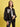 A woman with shoulder-length brown hair and a confident look wears the Sanctuary Clothing x PEANUTS 75th Anniversary right on jacket black over a white t-shirt and black pants, standing against a yellow background.