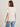 A woman with straight brown hair wears the arent gonna keep quiet tee in pink milk by Sanctuary Clothing x PEANUTS 75th Anniversary, paired with blue jeans, standing facing away from the camera against a neutral background.