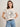 A woman with light skin and shoulder-length brown hair wears Sanctuary Clothing x PEANUTS 75th Anniversary's "the doctor is in tee collagen," a white T-shirt featuring the classic Peanuts "Psychiatric Help 5¢. The Doctor is IN." design.