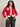 A woman with curly hair smiles, wearing the Sanctuary Clothing x PEANUTS 75th Anniversary joe cool zip up sweater in cherry lacquer, paired with high-waisted black jeans and a black belt. One hand is on her hip as she stands against a plain background.