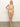 A woman poses barefoot against a plain backdrop wearing the Sanctuary Clothing's charming floral V wire bandeau in white, adorned with light colors highlighted by pink and green accents, one hand confidently placed on her hip.