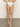A person models Sanctuary Clothing's "refresh rib high leg high rise white" bikini bottoms, standing with one leg crossed against a simple backdrop. The fabric has a ribbed texture, and the lighting is soft and even.