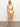 A woman stands barefoot against a plain background, wearing Sanctuary Clothing's stay connected high rise bikini bottom in daiquiri with a matching light yellow-green one-shoulder bikini top.