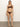 A person confidently stands on a neutral background wearing Sanctuary Clothing's espresso Stay Connected hipster bikini bottom. They have long hair and a calm expression, their feet slightly apart with arms relaxed, against a gray floor and plain off-white backdrop.
