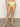 A person stands barefoot on concrete, wearing the Sanctuary Clothing stay connected high rise bikini bottom in daiquiri. Their upper body and face are not visible, with a plain light-colored wall in the background.