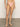A person wearing Sanctuary Clothing's "Stay Connected High Leg Hipster Bikini Bottom Cherry Blossom" stands on a gray floor against an off-white wall, highlighting the peach-colored bikini bottom with small side bows and showcasing its fit and design.