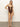 A woman poses confidently in a "stay connected open front mio swimsuit" by Sanctuary Clothing. This espresso-colored one-piece features three cut-out sections linked by decorative rings. She stands barefoot on a neutral background, right hand on her hip, with long hair over her shoulders.