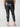 A person is shown from behind, wearing Sanctuary Clothing's Runway Legging Black from the Inclusive Collection. They are also wearing a green top and black heeled sandals featuring a cork-like pattern on the heels. The image captures the lower back down to the feet, highlighting the tight fit of the leggings.