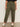 A person stands against a plain light background wearing Sanctuary Clothing's boyfriend utility pant kalamata extended sizing with large front pockets, paired with a black t-shirt and white sneakers featuring black accents. Their arms are relaxed by their sides.