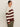 A person stands sideways against a light background, wearing the Sanctuary Clothing 24 7 Popover Chicory Light Oat sweater in extended sizing with olive green pants. Their dark hair is pulled back and they have a neutral expression.