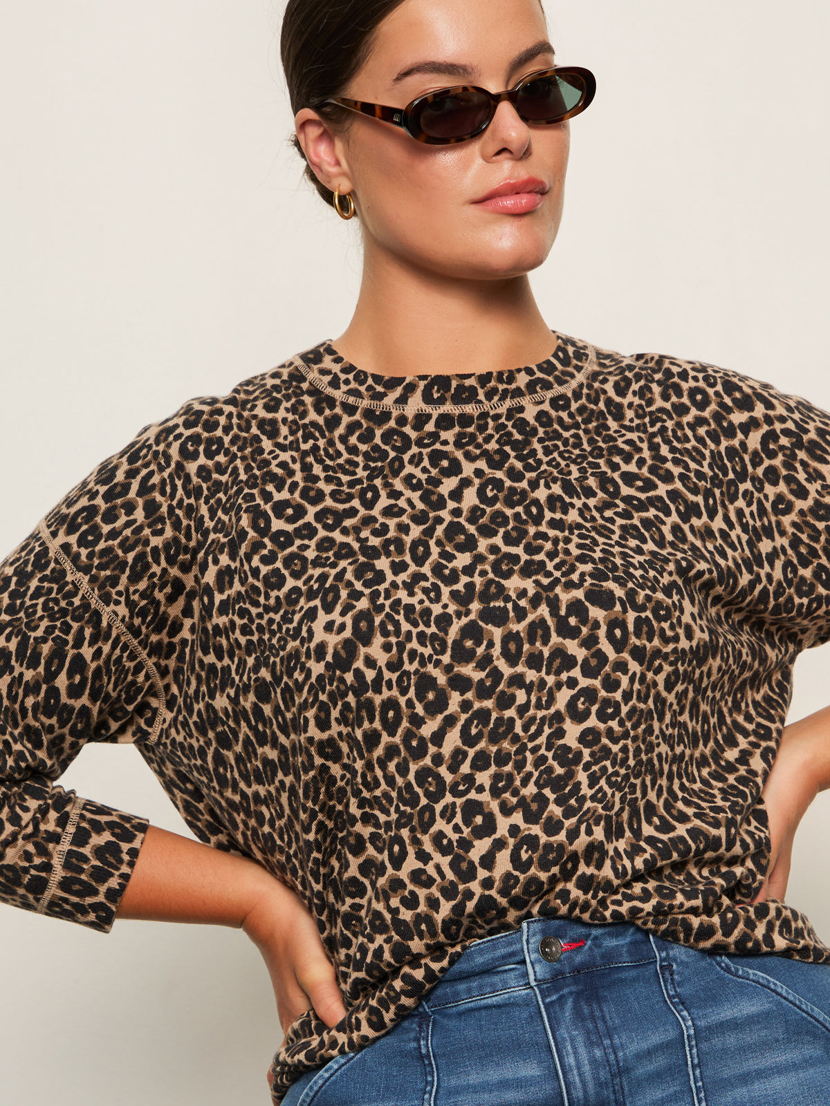 A woman in the Sanctuary Clothing 24 7 popover french kitty top and blue jeans poses confidently against a plain light background, wearing dark sunglasses.