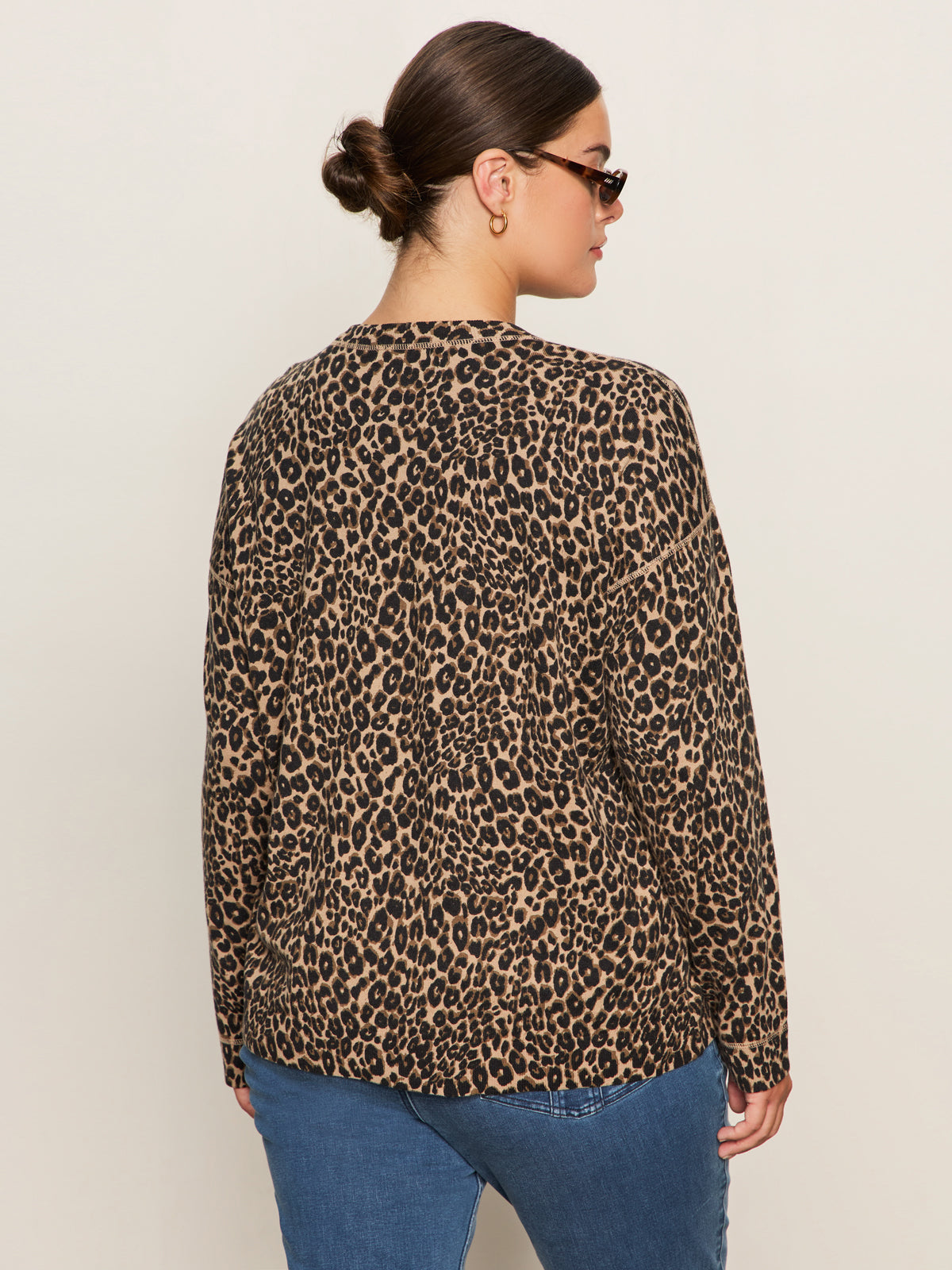 A person faces away from the camera against a plain light background, wearing sunglasses, blue jeans, and the Sanctuary Clothing 24 7 Popover French Kitty top in extended sizing.