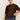 A woman with dark hair in a low bun wears gold hoop earrings, blue jeans, and the Sanctuary Clothing perfect sweater tee chicory extended sizing, standing against a light background and holding her sweater with one hand.