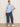 A woman stands against a beige wall, wearing the Sanctuary Clothing perfect sweater tee in blue powder (extended sizing), wide-leg blue jeans, and white sneakers. Her hair is tied back and one hand is in her pocket.