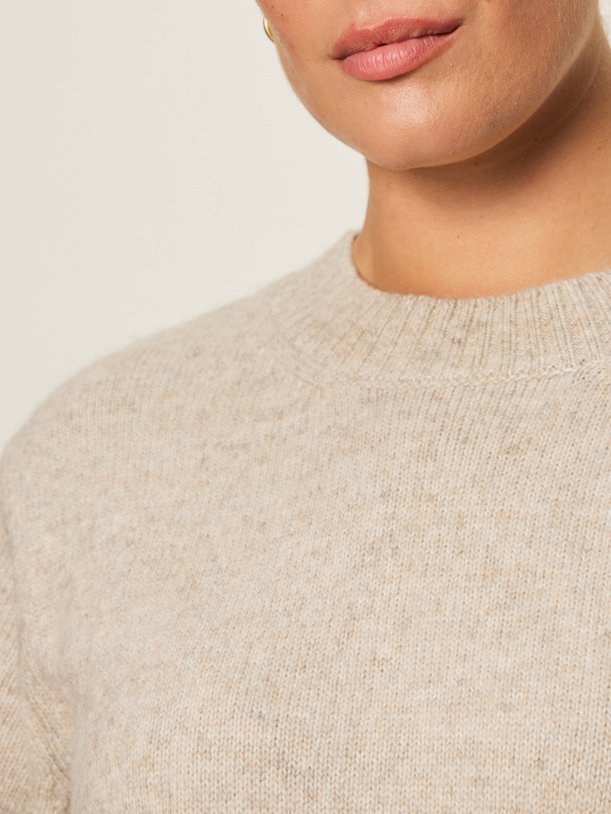 Close-up of a person wearing the Sanctuary Clothing perfect sweater tee in heather pearl (extended sizing), highlighting the knit texture. Only the lower face and upper chest are shown. The wearer has light skin and a subtle gold earring.