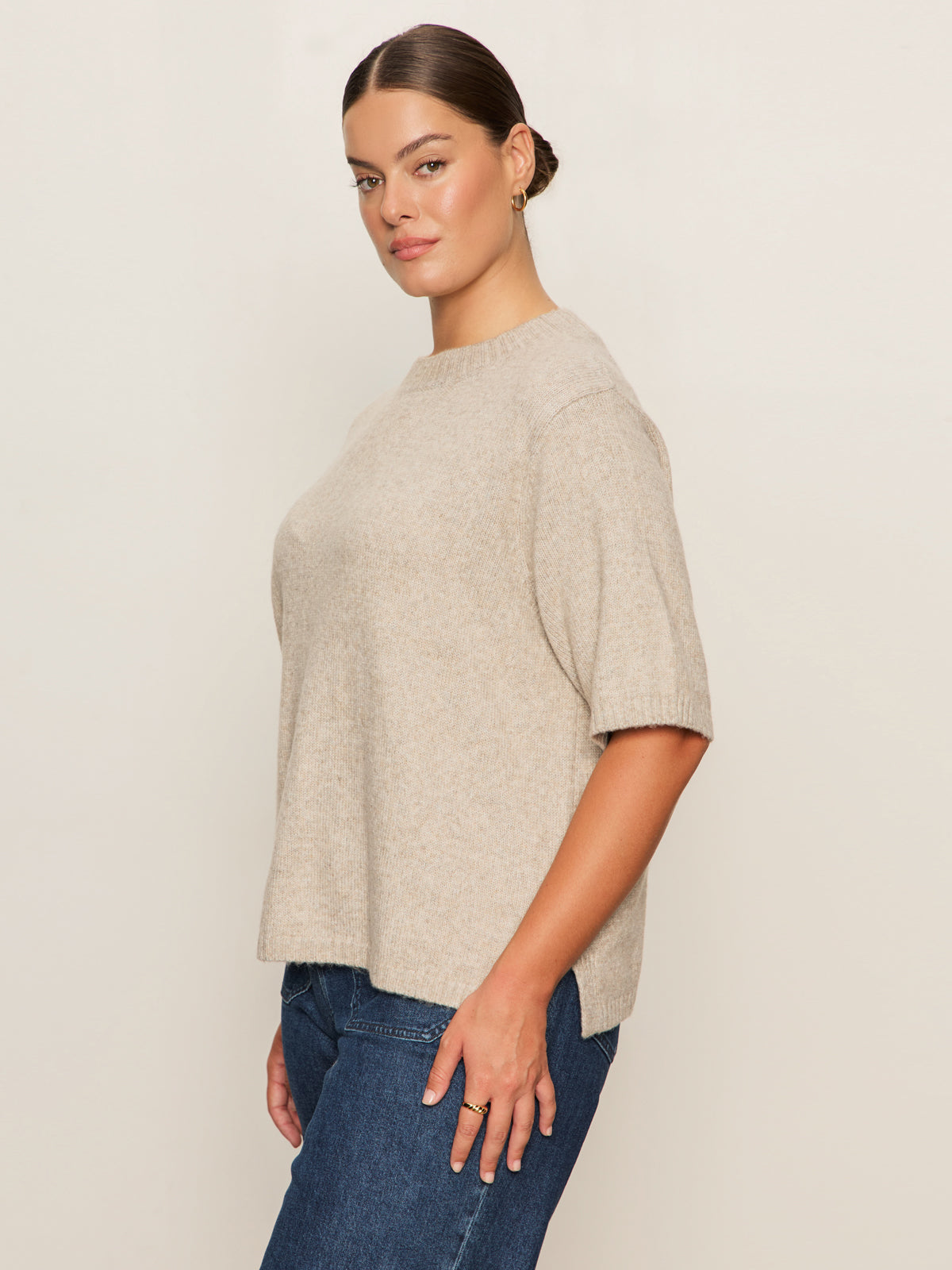Woman poses confidently in side profile against a light background, wearing the Sanctuary Clothing perfect sweater tee in heather pearl (extended sizing) and blue jeans, with her hair pulled back.