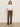 A woman in sunglasses, a white short-sleeve t-shirt, beige boots, and Sanctuary Clothing's corduroy hayden bootcut pant in kalamata stands facing forward against a plain light background.
