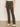 A person wearing Sanctuary Clothing's corduroy hayden bootcut pant in kalamata, paired with a tucked-in white shirt and beige shoes, stands indoors against a neutral wall and floor.