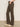 Someone wearing Sanctuary Clothing’s corduroy hayden bootcut pant in kalamata stands with one hand in their pocket against a plain light background, paired with beige pointed-toe heeled shoes.