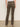 A person faces away, wearing Sanctuary Clothing's corduroy hayden bootcut pant in kalamata with a white top and heeled shoes, set against a plain light background.
