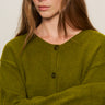 A woman with long brown hair wears the Sanctuary Clothing "must have cardi" in martini olive, featuring two buttons, and stands with her arms crossed against a plain background, looking directly at the camera.