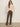 A woman stands against a plain background with her hands in her pockets, wearing sunglasses and the Sanctuary Clothing boheme popover light oat sweater, paired with brown high-waisted corduroy pants and light beige boots.