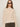 A woman with straight brown hair wears the Sanctuary Clothing boheme popover light oat sweater, round sunglasses, hoop earrings, and olive green pants against a plain light background.