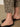 Close-up of a person wearing Sanctuary Clothing's cadence 90 straight crop jeans in the French Kitty print, featuring a black leopard pattern, standing on a neutral floor with black slip-on sandals.