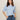 A woman with straight brown hair wears the Sanctuary Clothing perfect sweater tee in blue powder and high-waisted blue jeans with a brown belt, standing against a plain light background with her hands in her pockets.