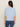 A woman with long brown hair, seen from behind, wears the Sanctuary Clothing "perfect sweater tee" in blue powder and blue jeans, standing against a plain light background.