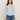 A woman with straight brown hair wears the Sanctuary Clothing dreamgirl lace button up top in blue powder and blue jeans, standing against a beige background and looking at the camera with a neutral expression.