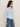 A woman stands sideways wearing the Sanctuary Clothing Dreamgirl Lace Button Up Top in blue powder with blue jeans, set against a plain, neutral background.