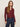 A woman with long brown hair wears the Sanctuary Clothing dreamgirl lace button up night berry shirt with high-waisted blue jeans, standing against a plain light background and gazing at the camera neutrally.