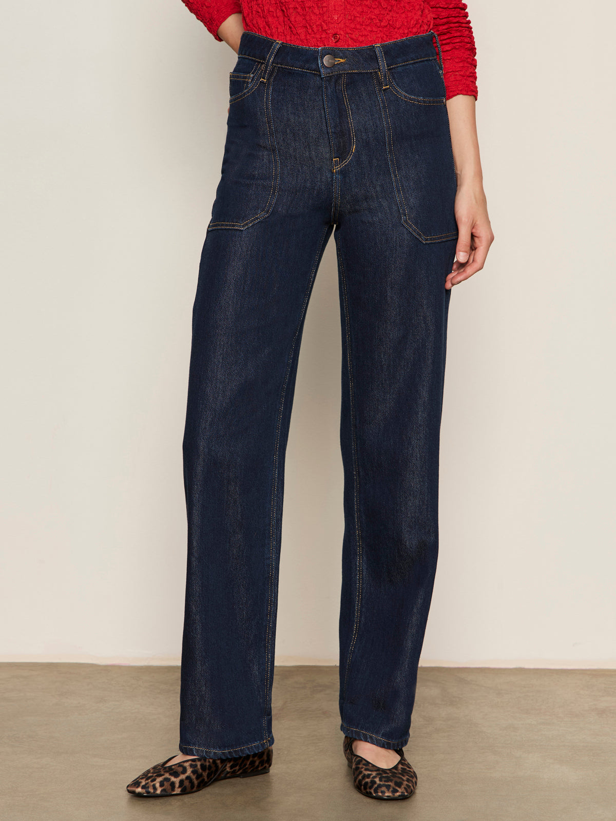 A person models the lower half, wearing Sanctuary Clothing’s soleil 90s straight jeans in indigo dark raw rinse, paired with a red textured top and leopard-print flats against a plain light background.
