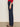 A person stands sideways in Sanctuary Clothing Soleil 90s Straight Jeans in indigo dark raw rinse, paired with a red textured long-sleeve top and leopard print flats against a plain light background.