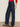 A person wearing Sanctuary Clothing's soleil 90s straight jeans indigo dark raw rinse, a red textured long-sleeve top, and leopard-print flats stands against a plain light-colored wall and floor.