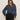 A woman with long brown hair wears black sunglasses, black pants, and the Sanctuary Clothing personal best blouse moonshadow—a loose-fitting blue denim button-up—standing against a plain light background with one hand in her pocket.