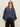 A woman with long light brown hair wears black sunglasses, black pants, and the Sanctuary Clothing personal best blouse in moonshadow. She stands against a plain light background with her hands in her pockets.